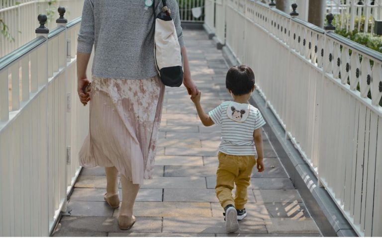 A busy mom carrying a tote bag and walking with a child stylo